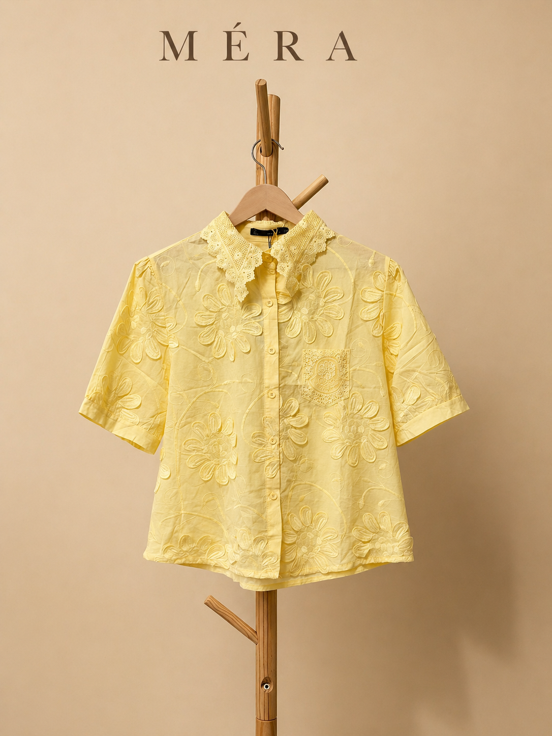 Yellow short-sleeve shirt on a wooden hanger against a beige background with 'Méra' branding.