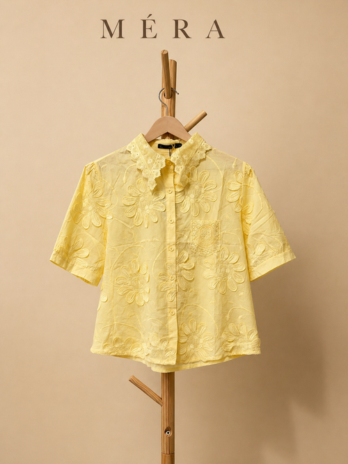 Yellow short-sleeve shirt on a wooden hanger against a beige background with 'Méra' branding.